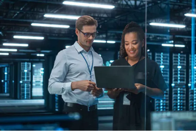 A man and a woman in a server room with a laptop